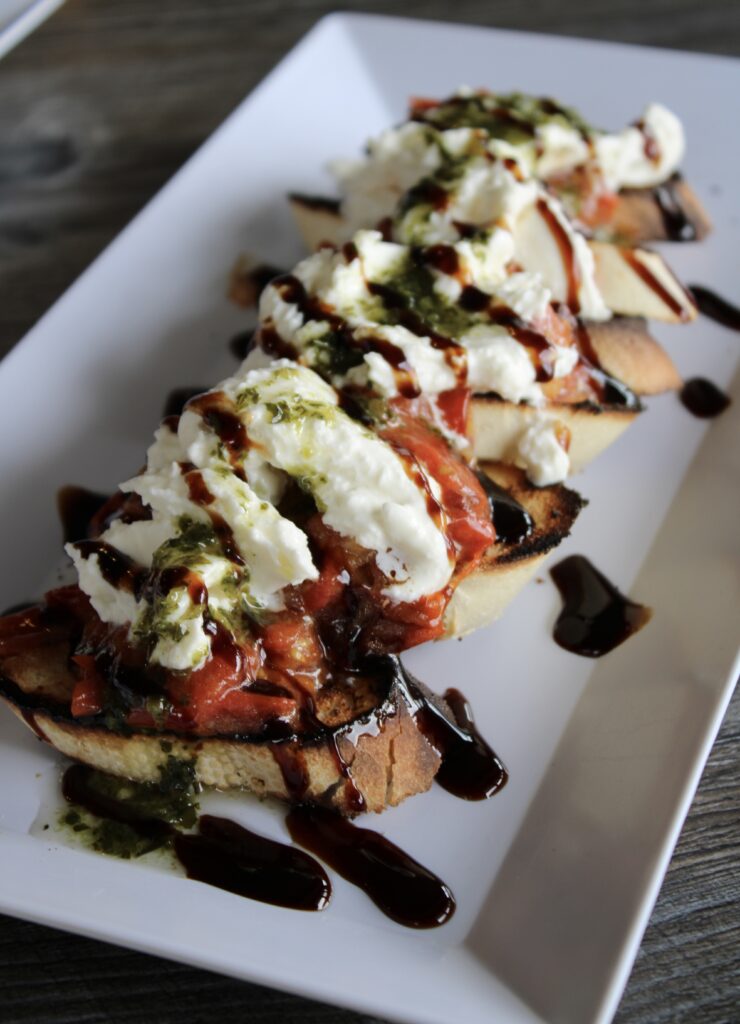 Tomato bruschetta with fresh burrata, basil oil, and balsamic glaze on toasted french bread at River Oaks Golf Course patio dining