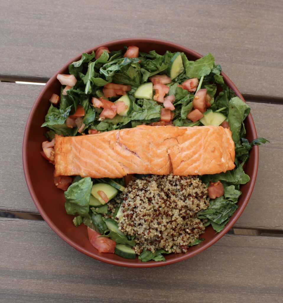 Grilled salmon fillet served over fresh greens with quinoa, cucumber, and tomatoes at River Oaks Golf Course patio dining