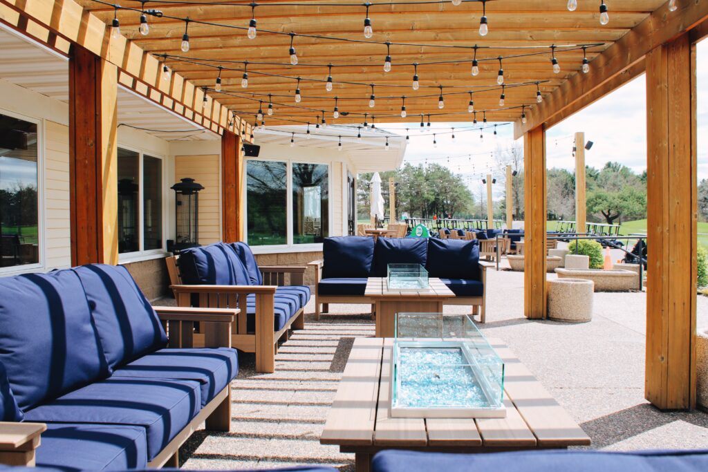 Covered outdoor patio seating with pergola, string lights, and lounge furniture at River Oaks Golf Course in Cottage Grove Minnesota