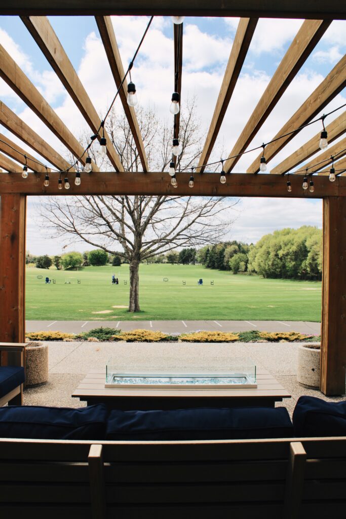 Pergola-covered patio seating with string lights overlooking golf course and driving range at River Oaks Golf Course in Cottage Grove Minnesota