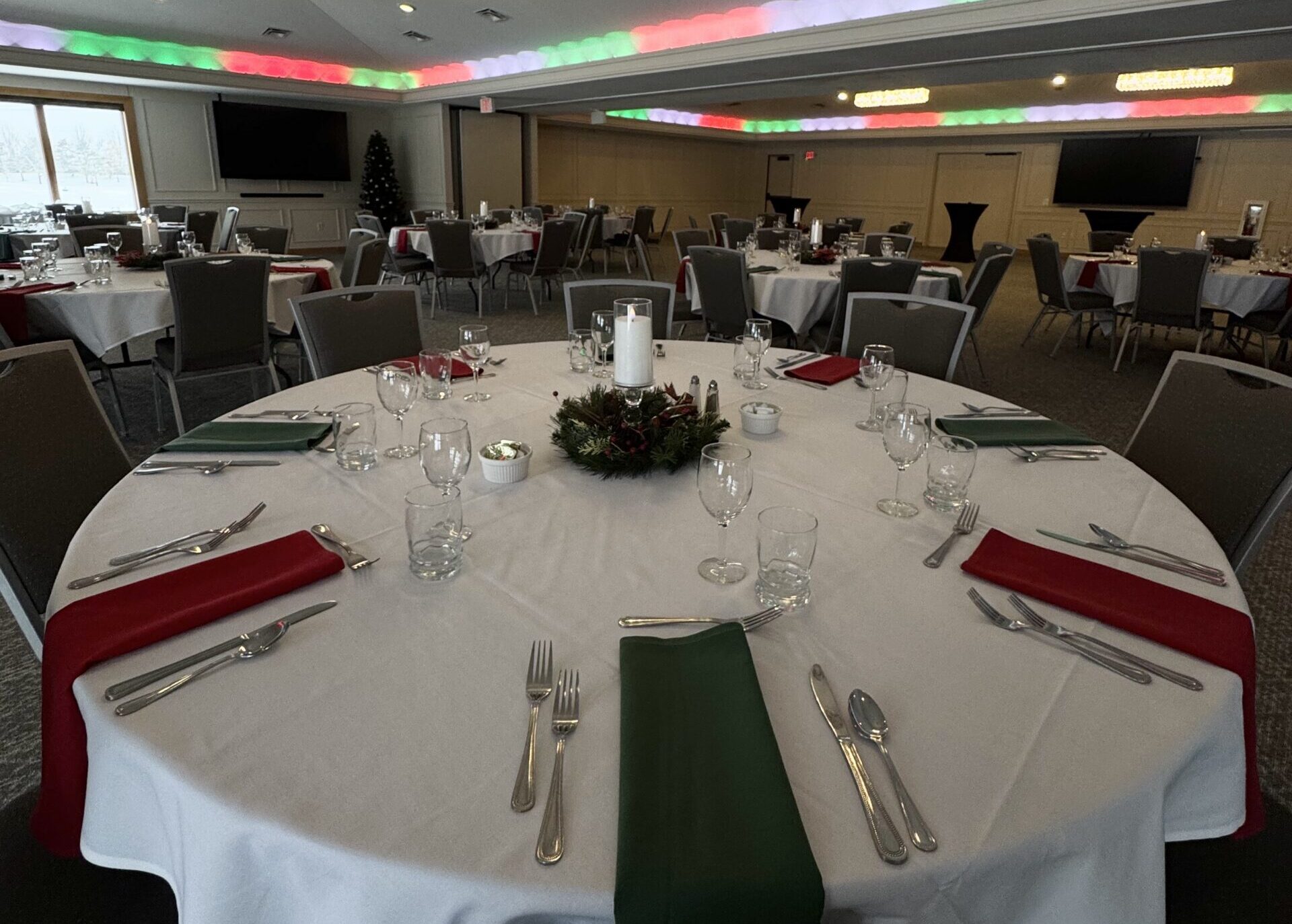 Elegant banquet room at River Oaks Golf Course & Event Center decorated for a holiday gathering, featuring round tables with festive red and green linens, crystal chandeliers, and customizable event lighting in Cottage Grove, Minnesota.