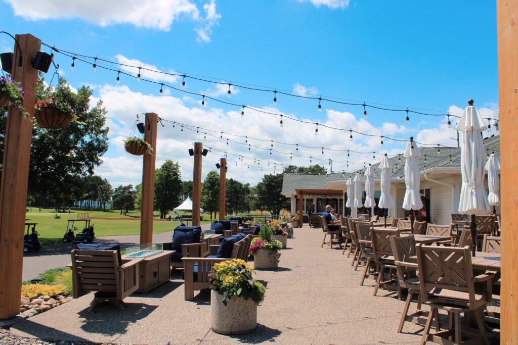 Spacious outdoor patio at River Oaks Golf Course and Event Center featuring dining tables, lounge seating, string lights, and scenic golf course views in Cottage Grove, Minnesota.