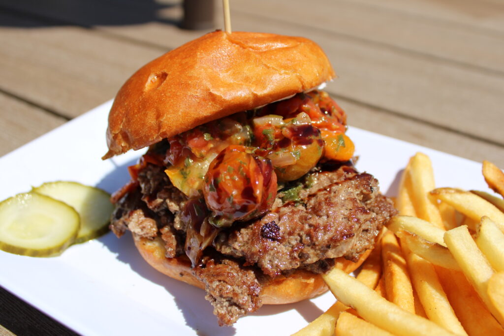 Boursin Bruschetta Burger served with french fries at Eagles Bar & Grill, featuring a double smash burger topped with Boursin cheese, roasted tomatoes, basil oil, and balsamic glaze on a toasted brioche bun.